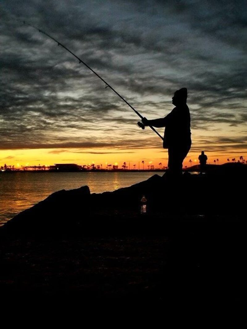 A man is fishing in the ocean at sunset.