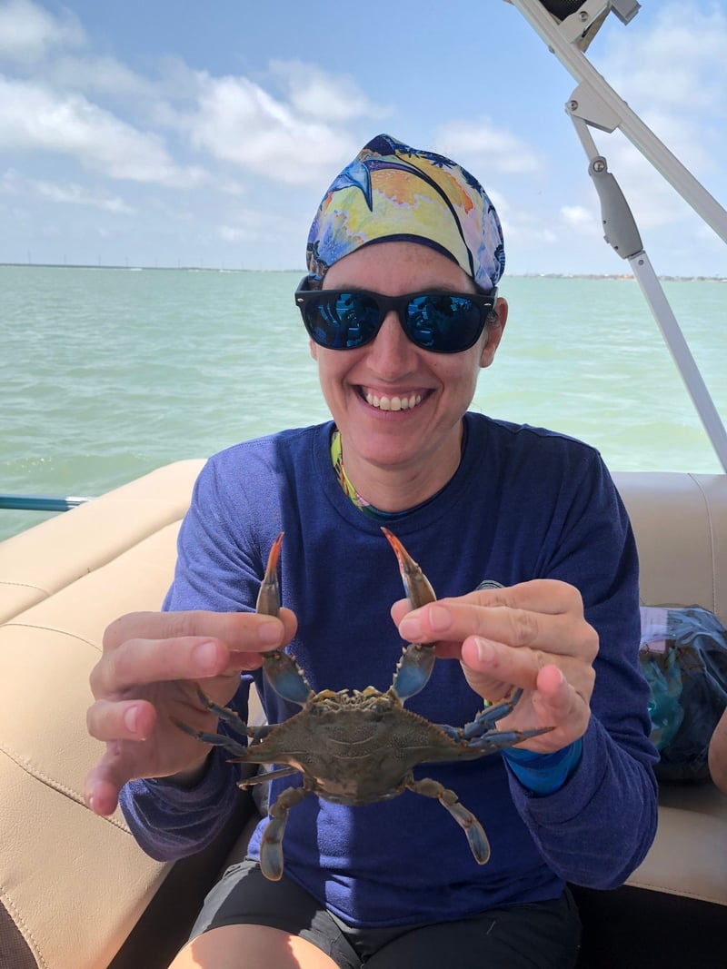 A woman is sitting on a boat holding a crab in her hands.