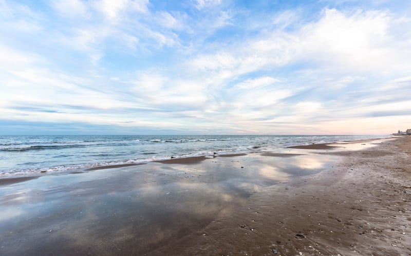 A beach with a blue sky and clouds reflected in the water