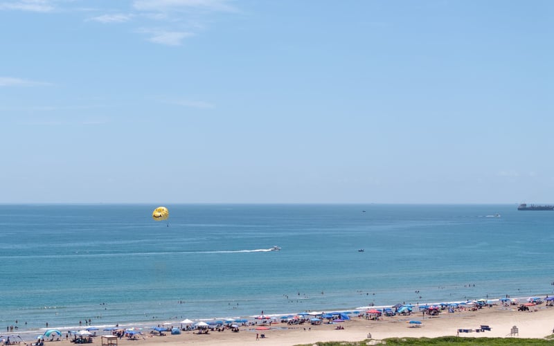 A view of a beach with umbrellas and a parachute in the distance.