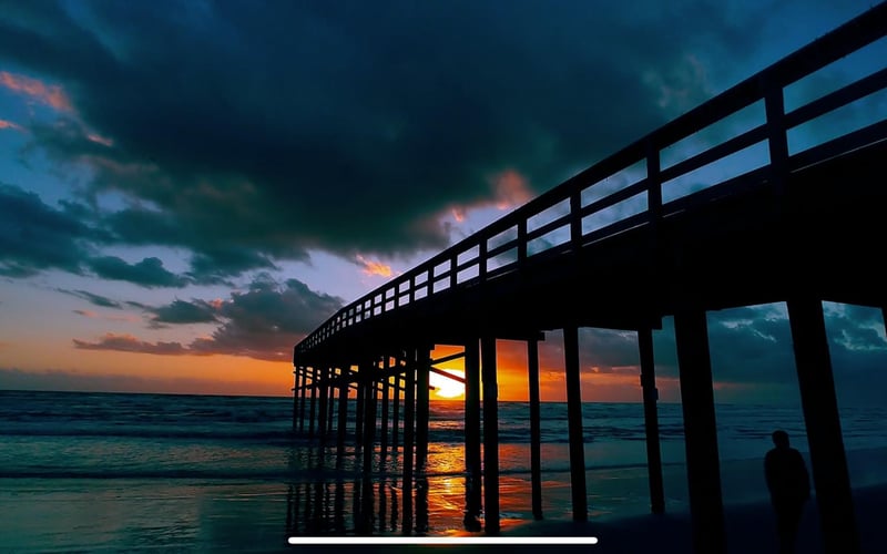 A pier overlooking the ocean at sunset with a person standing underneath it.