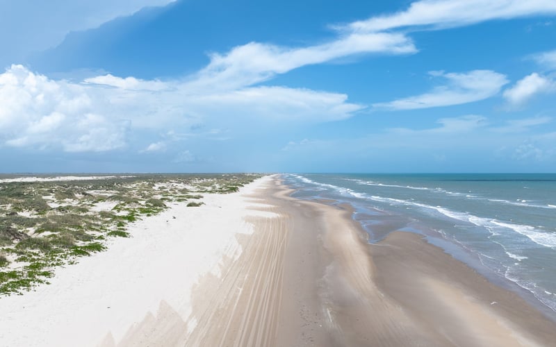 An aerial view of a long sandy beach leading to the ocean.