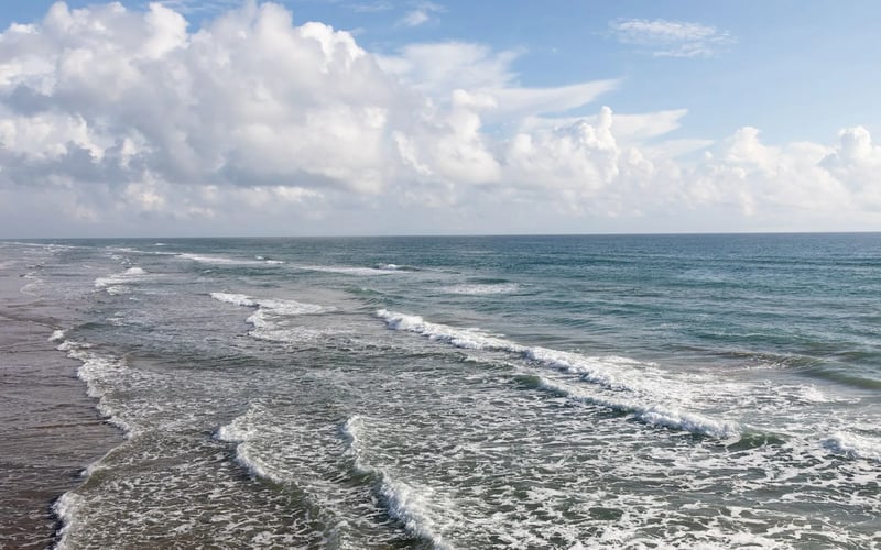 A beach with waves crashing against the shore on a cloudy day.