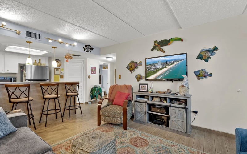 A living room with a couch , chair , television and bar stools.