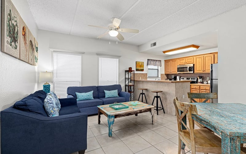 A living room with a blue couch , table , chairs and a ceiling fan.