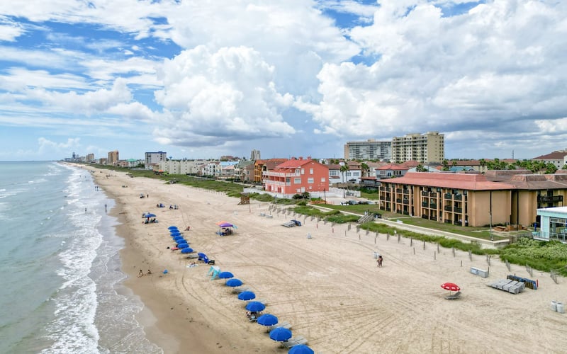 An aerial view of a beach with blue umbrellas and chairs.
