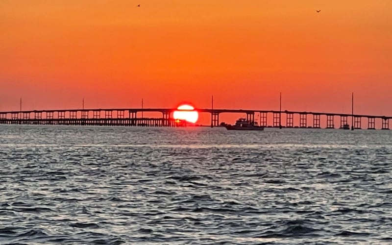 The sun is setting over a bridge over the ocean