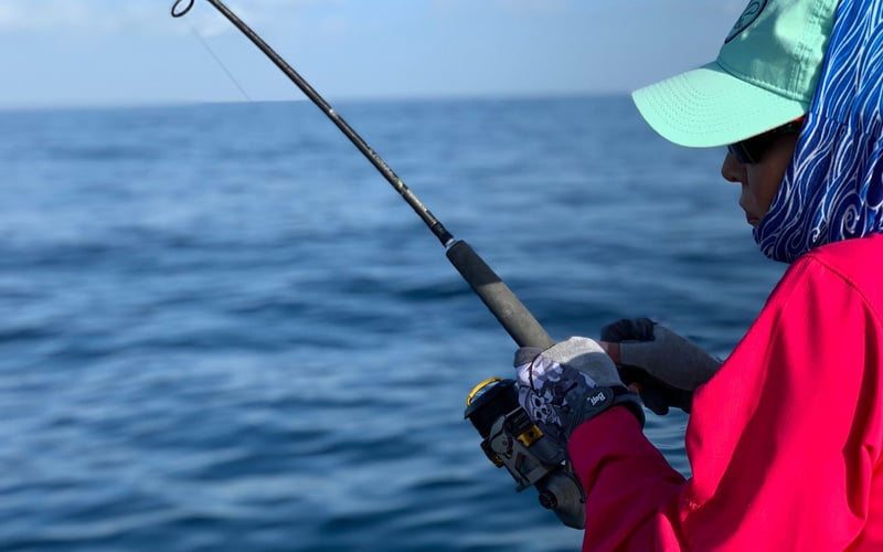 A woman in a pink jacket is fishing in the ocean