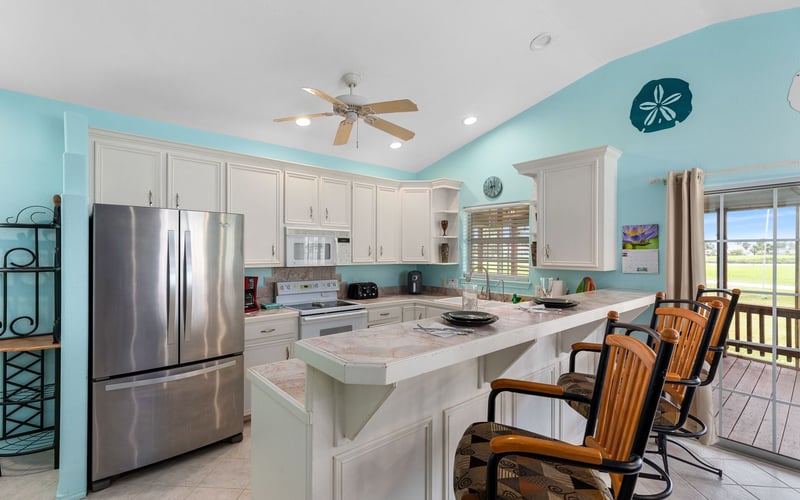 A kitchen with white cabinets , stainless steel appliances , a refrigerator and a bar.