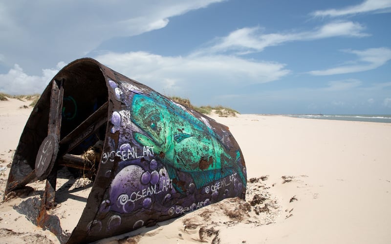 A large piece of metal is sitting on a sandy beach.